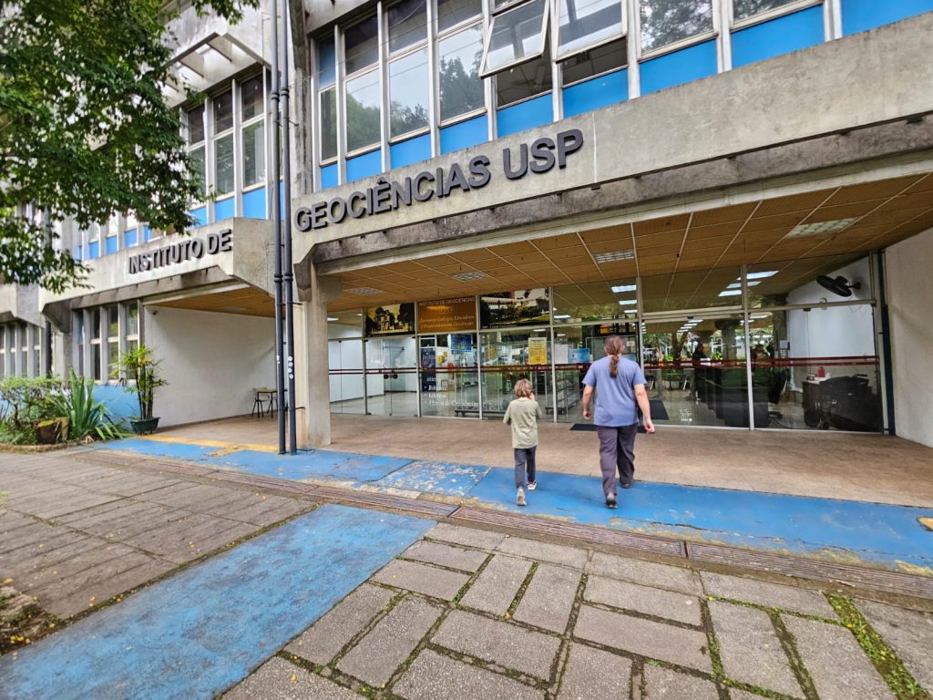 Fachada do Instituto de Geociências da USP, com duas pessoas caminhando em direção à entrada principal.